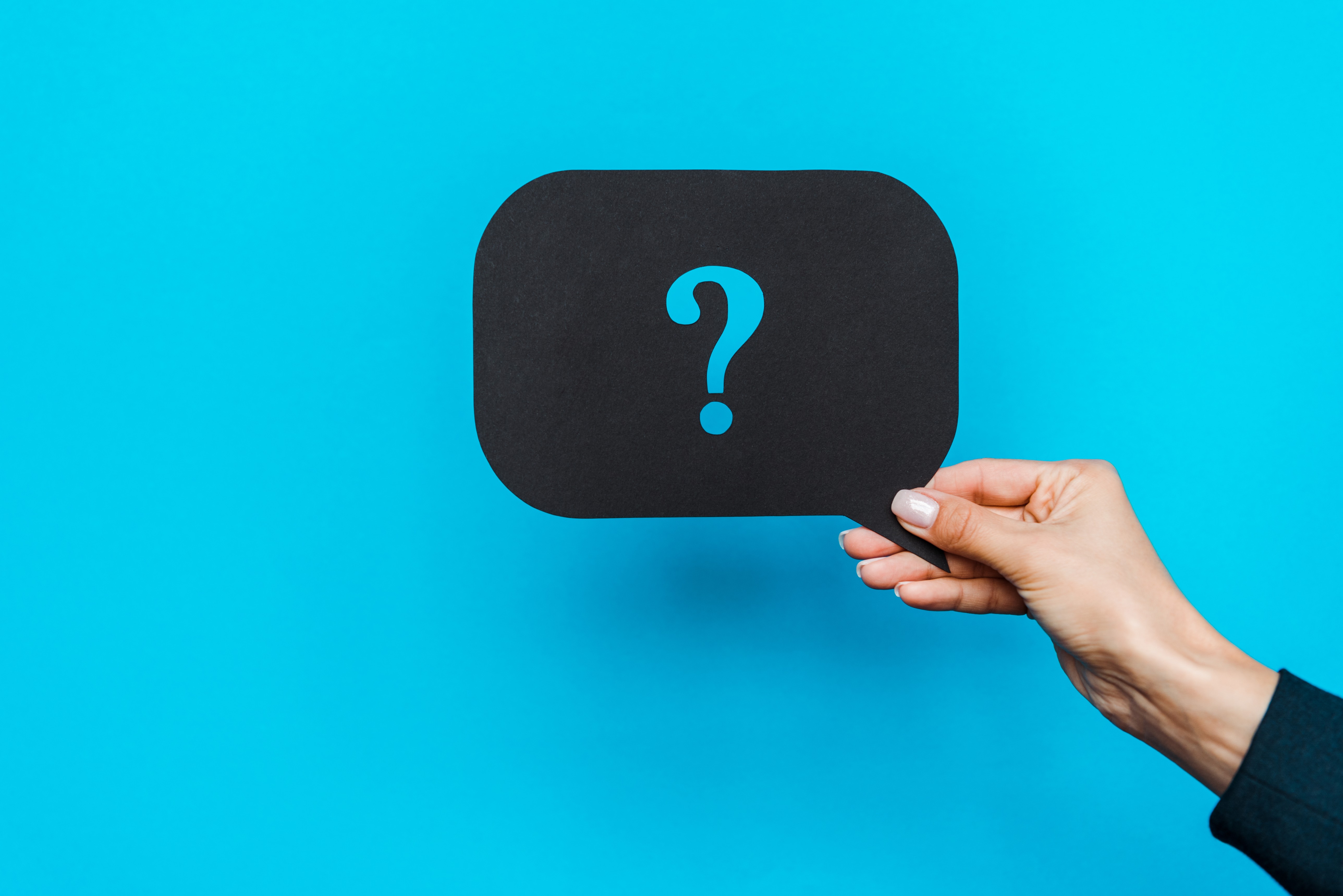 A woman's hand holds up a black speech bubble with a blue question mark against a bright blue background, representing the question of Meta ads attribution vs intelligence
