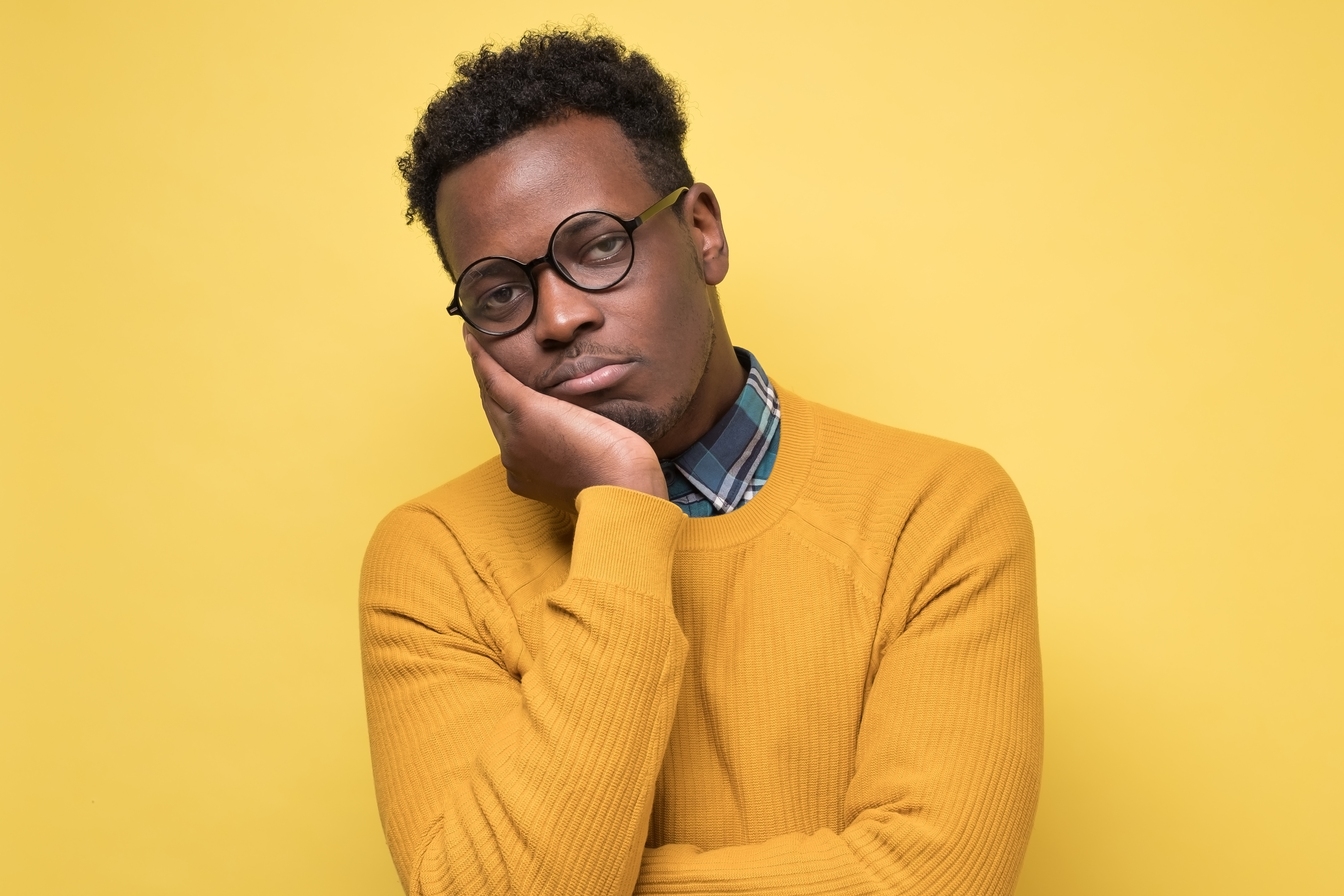 A visibly bored man in glasses resting his chin on his hand against a yellow background, representing Meta ads audience fatigue